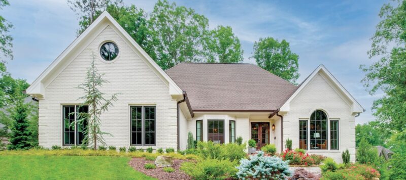 a brick home with a green, grassy yard that has lots of plants in it