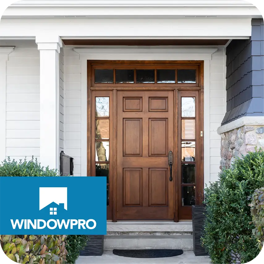 Front view of a house entrance featuring a rich wooden door with side and transom windows, surrounded by white trim and shrubs